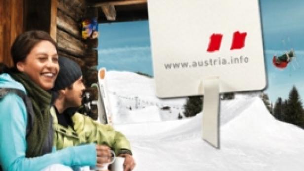 Ein Paar entspannt vor einer Hütte im Schnee, im Hintergrund ein Schild mit der Aufschrift „It's got to be Austria“.