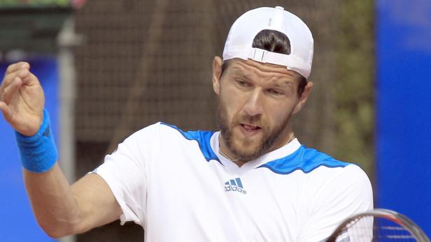 Ein Tennisspieler mit Bart und weißer Kappe gestikuliert auf dem Platz.