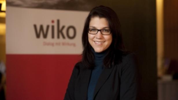 Eine Frau mit Brille lächelt vor einem Wiko-Banner.
