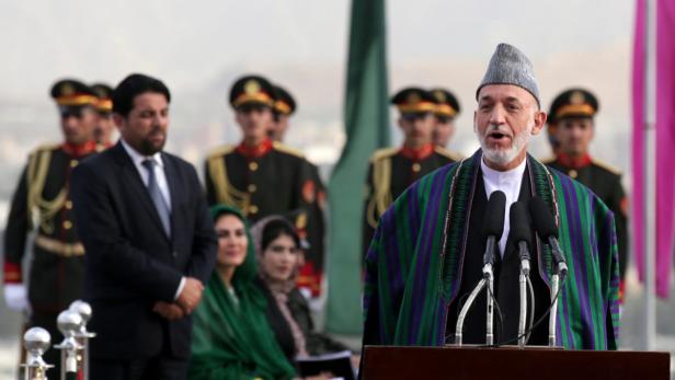 Hamid Karzai hält eine Rede vor einer Menschenmenge und Soldaten im Hintergrund.