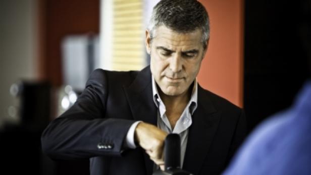 George Clooney bedient eine Kaffeemaschine.