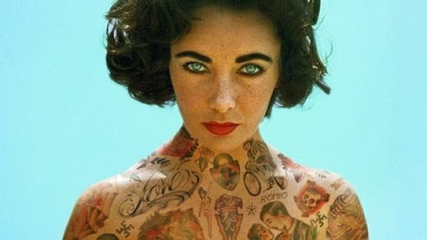 Elizabeth Taylor mit zahlreichen Tätowierungen auf Oberkörper und Armen vor blauem Hintergrund.
