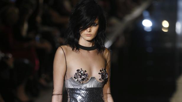 Ein Model mit dunklen Haaren trägt ein silbernes Paillettenkleid mit transparentem Oberteil.