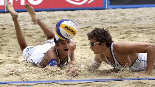 Zwei Beachvolleyballspieler hechten nach einem Ball im Sand.