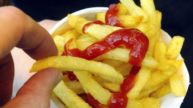 Eine Hand nimmt eine Pommes Frites aus einer Schale mit Ketchup.