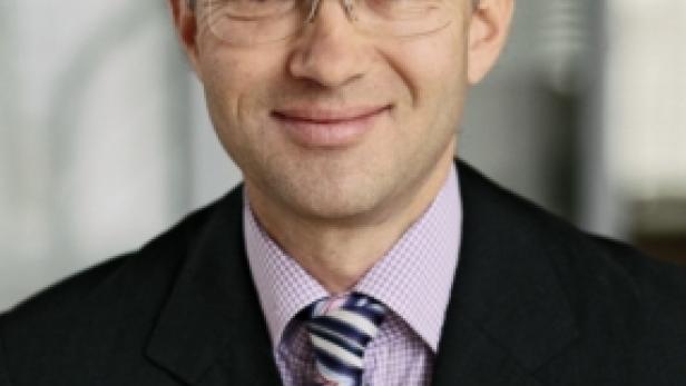 Ein Mann mit Brille, Anzug und Krawatte blickt in die Kamera.