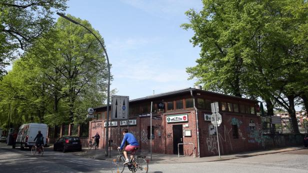 Ein Backsteingebäude mit dem Schriftzug „Hütte“ an einer Straßenecke mit Radfahrern.