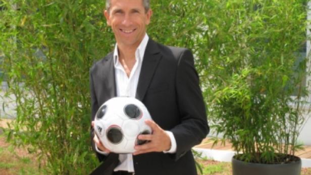 Ein Mann im Anzug hält einen Fußball in seinen Händen.