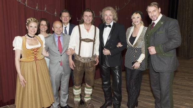 Eine Gruppe von Personen posiert vor einem roten Vorhang, einige in Tracht.