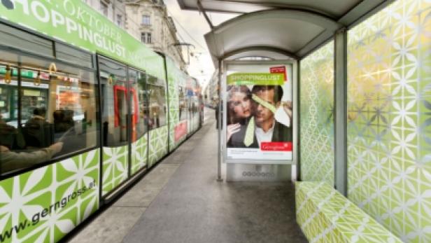 Eine Straßenbahnhaltestelle mit Werbung für „Shoppinglust“ und einem Zug mit Werbung für Gerngross.