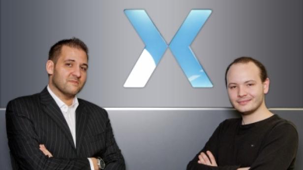 Zwei Männer stehen vor einem grauen Hintergrund mit einem blauen „X“-Logo.
