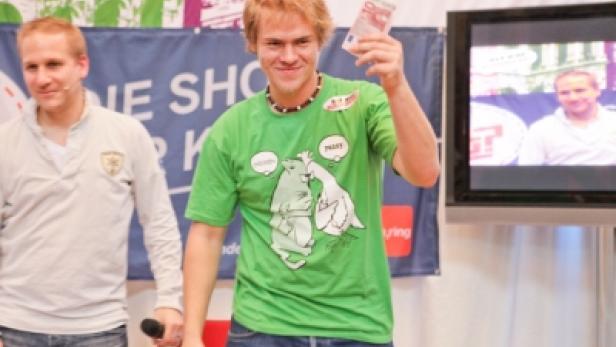Ein junger Mann im grünen T-Shirt hält einen Geldschein in die Höhe.
