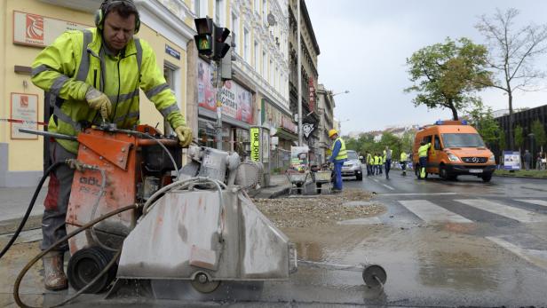 Ein Bauarbeiter schneidet mit einer Steinsäge Asphalt auf einer Straße.