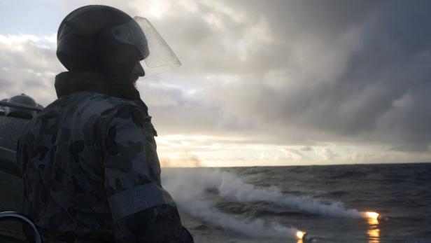 Ein Soldat in Tarnuniform und Helm steht auf einem Schiff und blickt auf das Meer.