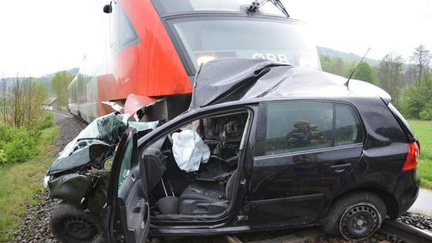 Ein schwarzer PKW ist mit einem roten Zug auf einem Bahnübergang kollidiert.