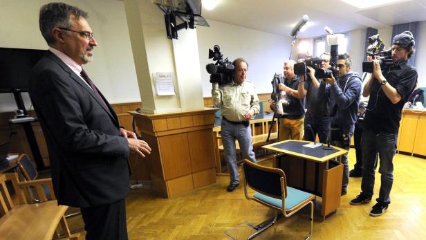 Ein Mann im Anzug steht vor einer Gruppe von Kameraleuten in einem Raum.