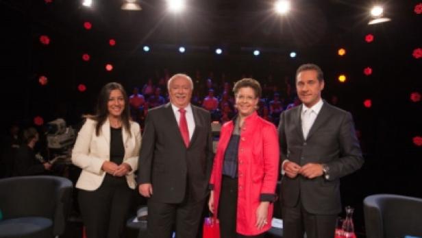 Vier Personen stehen in einem Fernsehstudio vor einem Publikum.