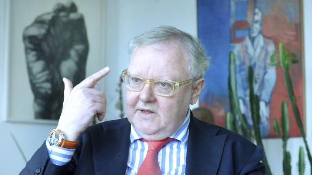 Ein Mann mit Brille und Anzug gestikuliert vor zwei Gemälden.