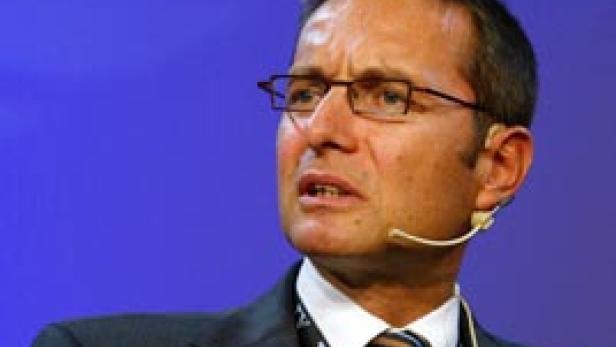 Ein Mann mit Brille und Anzug spricht vor einem blauen Hintergrund.