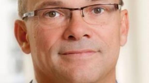 Ein Mann mit Brille und Anzug blickt in die Kamera.