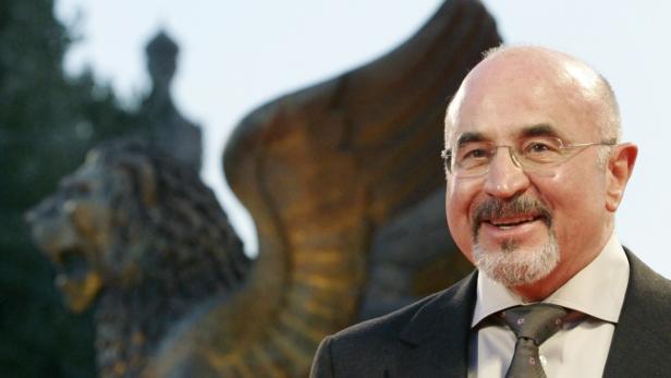 Ein lächelnder Mann mit Brille vor einer Löwenstatue.