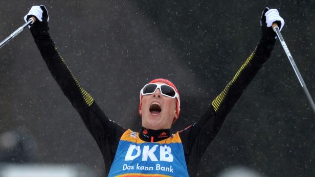 Ein jubelnder Skilangläufer mit Startnummer und Skibrille reißt die Arme hoch.