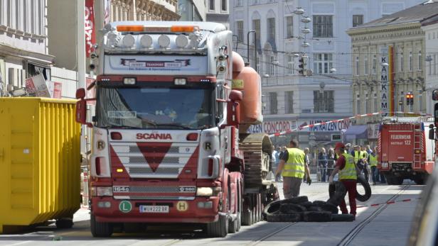 Ein Scania-Lkw transportiert eine Baumaschine durch eine Stadt.