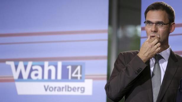Ein Mann mit Brille steht vor einem Wahlplakat für die Wahl 14 in Vorarlberg.