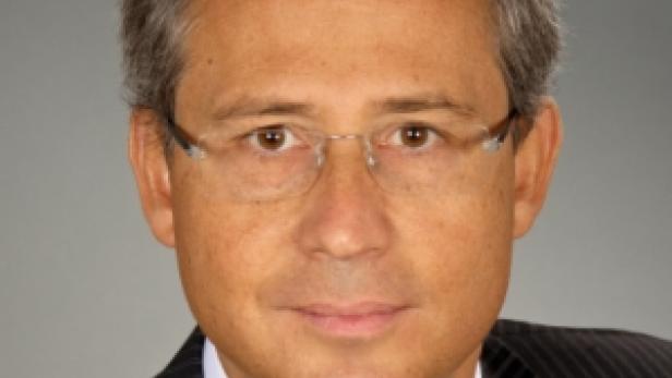 Ein Mann mit Brille und Anzug vor einem grauen Hintergrund.