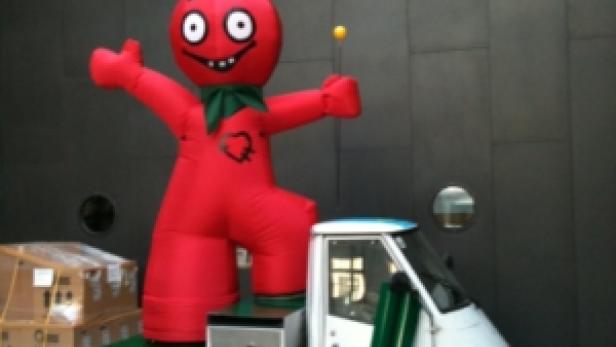 Eine rote, aufblasbare Figur steht auf der Ladefläche eines kleinen Lieferwagens von HDI Versicherung.