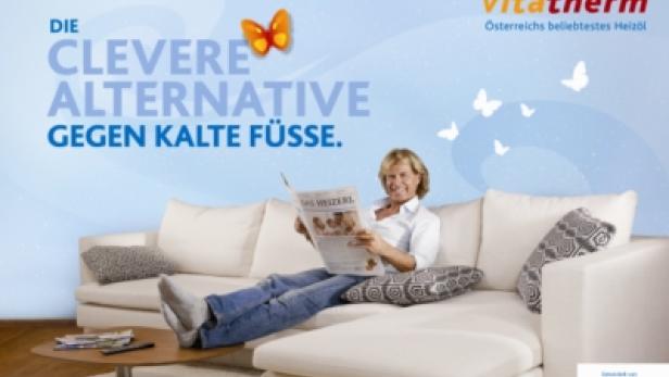 Eine Frau liest entspannt auf einem Sofa eine Zeitung; Werbung für „vitatherm“-Heizöl.
