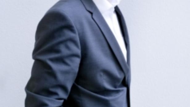 Ein Mann mit Brille und Anzug steht vor einer hellen Wand.