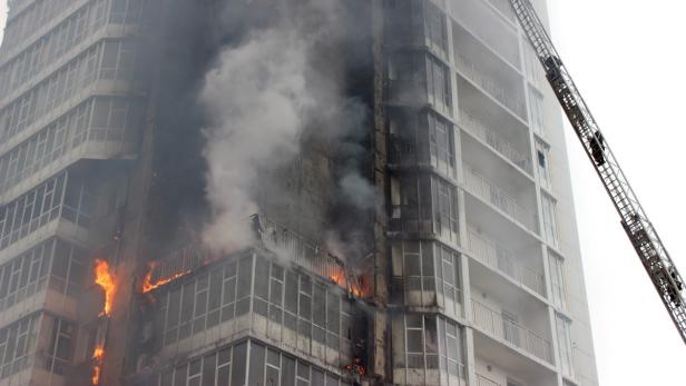 Ein Hochhaus steht in Flammen, dichter Rauch steigt auf. Eine Drehleiter ist im Einsatz.