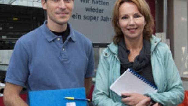 Zwei Personen stehen vor einem Bildschirm mit der Aufschrift „Wir hatten wieder ein super Jahr“.