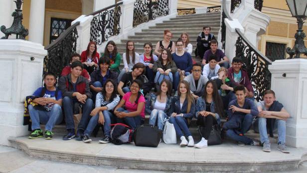 Eine Gruppe von Teenagern sitzt auf einer Treppe vor einem Gebäude.
