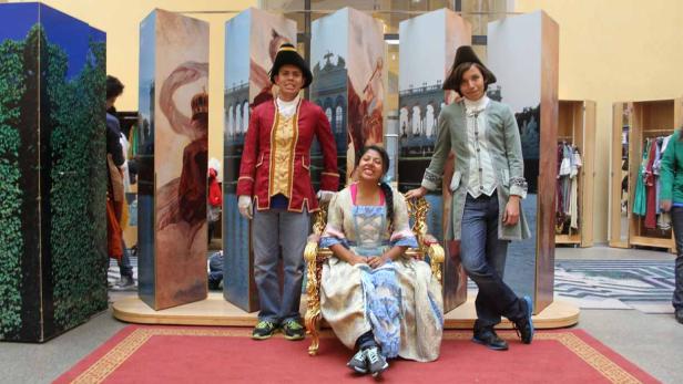 Drei Personen in historischen Kostümen posieren vor bemalten Kulissen.