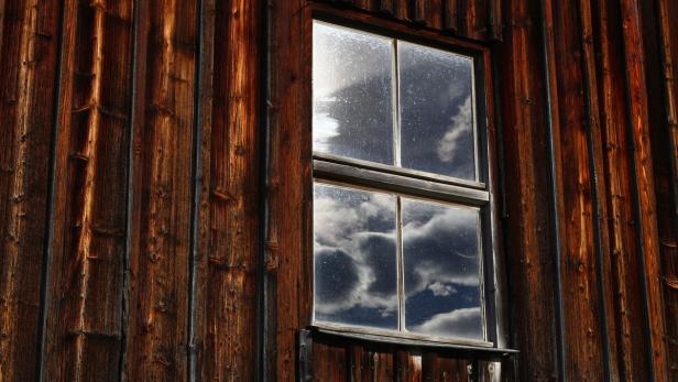 Ein Fenster spiegelt den Himmel mit Wolken in einer Holzwand.