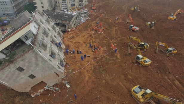 Ein eingestürztes Gebäude liegt auf einer Schlammlawine, während Rettungskräfte und Bagger im Einsatz sind.