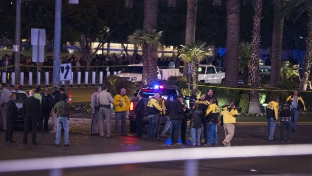 Polizisten untersuchen einen Tatort mit einem Polizeiauto und Absperrband im nächtlichen Las Vegas.