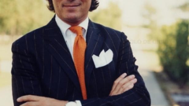 Ein Mann mit verschränkten Armen in einem eleganten Anzug mit orangefarbener Krawatte.