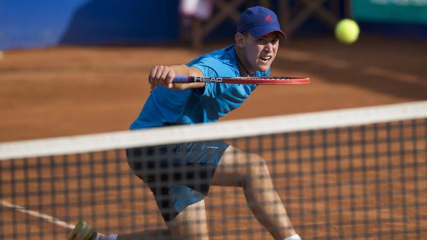 Ein Tennisspieler schlägt den Ball auf einem Sandplatz.