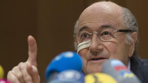 Sepp Blatter mit einem Pflaster über dem Auge gestikuliert vor Mikrofonen.