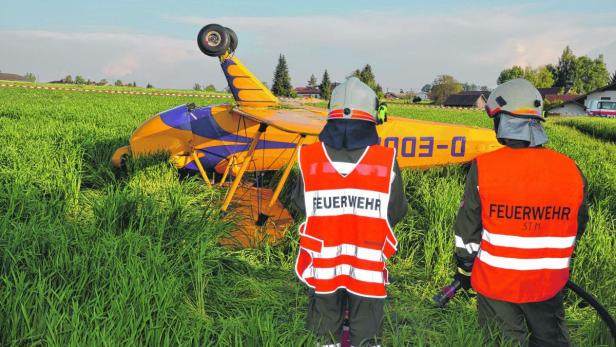 Ein gelbes und blaues Kleinflugzeug ist in einem Feld notgelandet, Feuerwehrleute stehen bereit.