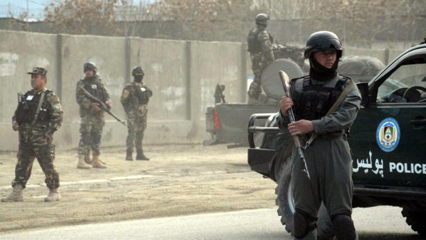 Bewaffnete Polizisten stehen vor einem Polizeifahrzeug in einer staubigen Straße.