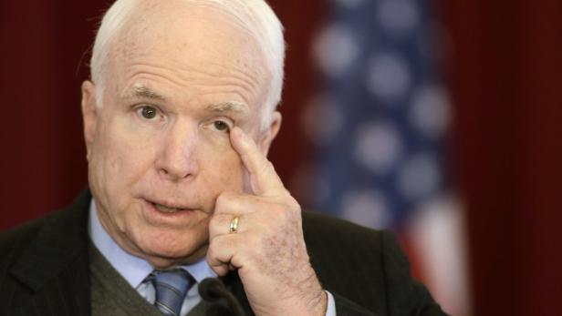 John McCain berührt sein Auge vor einer amerikanischen Flagge.