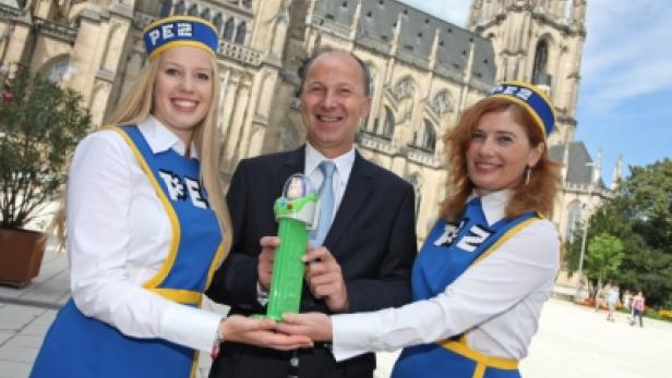 Ein Mann im Anzug präsentiert mit zwei PEZ-Mitarbeiterinnen einen PEZ-Spender vor dem Linzer Mariendom.