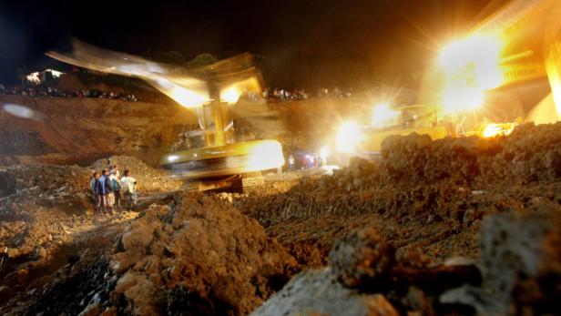 Bei Nacht beobachten Menschen Bagger bei der Arbeit in einer Baugrube.