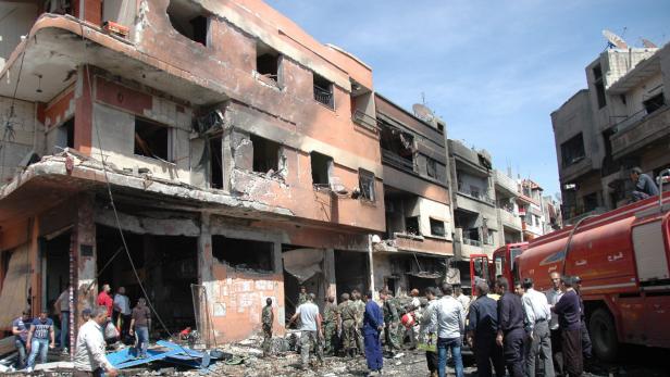 Ein beschädigtes Gebäude in einer Stadt, umgeben von Menschen und einem Feuerwehrauto.