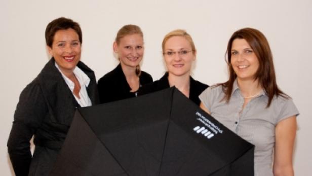 Vier Frauen posieren hinter einem schwarzen Regenschirm mit dem Aufdruck „Messemer Professional“.