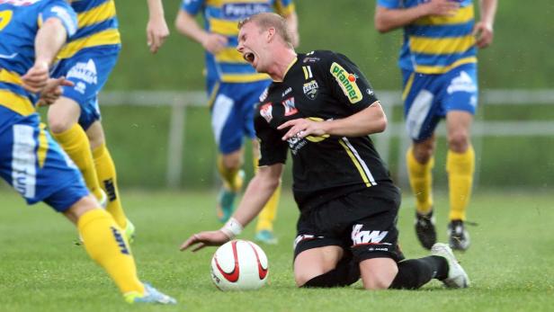 Ein Fußballspieler kniet auf dem Rasen, während er sich vor Schmerzen krümmt.